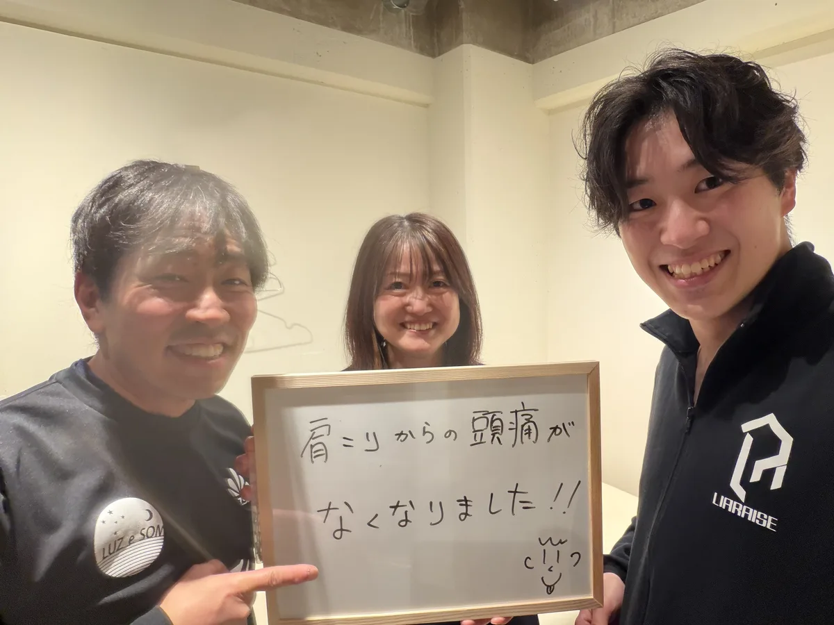 「肩こりからの頭痛がなくなりました!!」と書いたホワイトボードを持つご夫婦と野田